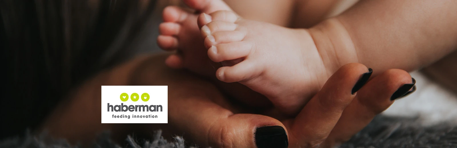 Adult female hand holding babies feet, Haberman logo positioned bottom left.