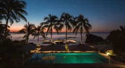 Pool with palm trees by the sea at sunset